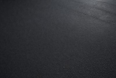 The primary subject of the image is a black asphalt road. The setting is a dark, empty street with no visible vehicles or people. The visual style is a photo, and the colors and mood are dark and moody.