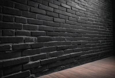 The primary subject of the image is a black brick wall. The setting is a dark room with a brick wall as the main focus. The visual style is a photo, and the dominant colors are black and grey, creating a moody atmosphere.