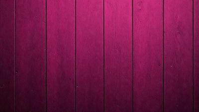 The primary subject of the image is a wooden wall with a purple color. The setting is a room with a wooden surface, and the visual style is a close-up of the wooden wall. The dominant colors are purple and brown, creating a warm and inviting atmosphere.