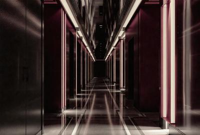 The image is a black and white photo of a long hallway with a row of doors. The hallway is illuminated by a row of lights, creating a dramatic atmosphere. The lights are positioned at regular intervals, providing a sense of depth and perspective to the scene. The overall mood of the image is one of mystery and intrigue, as the viewer is drawn into the depths of the hallway.