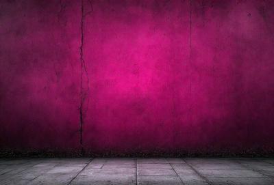 The primary subject of the image is a large, pink wall. The setting is a room with a concrete floor. The visual style is a photo, and the dominant colors are pink and red. The overall atmosphere is bold and striking, with the pink wall standing out against the concrete floor.