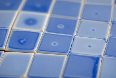 The primary subject of the image is a blue tile with a pattern of white dots. The setting is a bathroom, as the tiles are placed on a blue bathroom wall. The visual style is a photo, capturing the intricate pattern of the blue and white tiles. The colors and mood of the image are predominantly blue and white, creating a clean and soothing atmosphere.