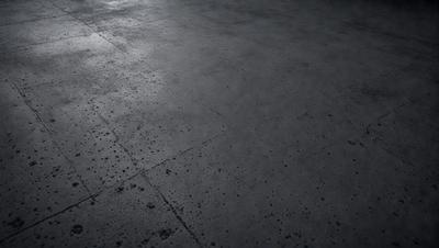 The primary subject of the image is a large, dark grey concrete floor. The setting is a room with a concrete surface, and the visual style is a black and white photo. The colors and mood of the image are dark and moody, with the concrete floor being the main focus.