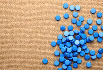 The primary subject of the image is a pile of blue plastic buttons. The buttons are scattered on a surface, which appears to be a brown cloth or a carpet. The visual style of the image is a close-up of the buttons, showcasing their details and colors. The overall atmosphere of the image is casual and playful, as the buttons are arranged in a relaxed manner.