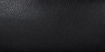 The primary subject of the image is a close-up of a black leather material. The setting is a black background, which provides a contrasting and dramatic effect. The visual style is a realistic representation of the leather material, showcasing its texture and appearance. The colors and mood of the image are predominantly dark and moody, with the black leather material being the main focus.