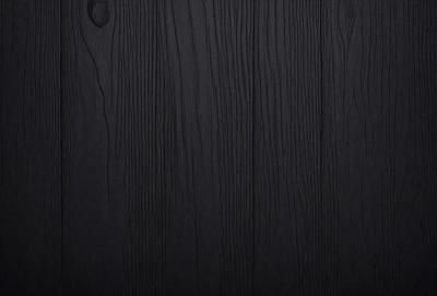 The primary subject of the image is a wooden wall. The setting is a dark room, and the visual style is a black and white photo. The colors and mood of the image are predominantly dark and moody, with the wooden wall being the main focus.