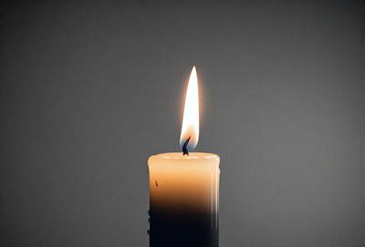 The primary subject of the image is a lit candle. The candle is placed on a white surface, which serves as the setting or background. The visual style of the image is a photo, capturing the candle's flame and the surrounding white background. The colors in the image are predominantly white, which creates a calm and serene atmosphere.