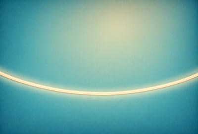 The primary subject of the image is a long, brightly lit yellow line that appears to be a light source. The setting is a blue wall, which serves as the background for the yellow line. The visual style of the image is a combination of a photo and a digital art, as it captures the light source's reflection on the blue wall. The colors and mood of the image are predominantly blue and yellow, creating a warm and inviting atmosphere.