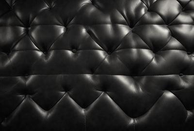 The primary subject of the image is a black leather couch with a black and white pattern. The couch is set against a black background, giving it a bold and striking appearance. The visual style of the image is a close-up of the couch, emphasizing its texture and pattern. The colors and mood of the image are predominantly black, creating a sleek and modern look.