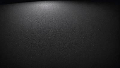 The primary subject of the image is a black surface, which appears to be a piece of cloth or a piece of black material. The setting is a dark room, and the visual style is a close-up of the black surface. The colors and mood of the image are predominantly dark and moody, with the black surface being the main focus of the image.