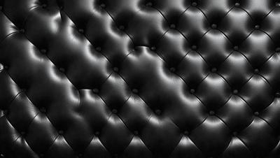 The primary subject of the image is a black leather couch. The setting is a room with a black background, which creates a striking contrast with the couch. The visual style is a close-up of the couch, showcasing its texture and details. The colors and mood of the image are predominantly black, giving it a sleek and modern appearance.