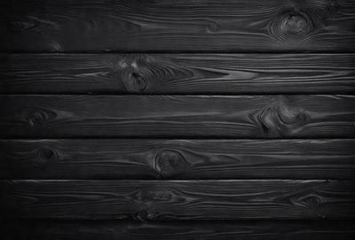 The primary subject of the image is a wooden wall with a black background. The setting is a room with a wooden wall, and the visual style is a black and white photo. The dominant colors are black and white, creating a moody atmosphere.