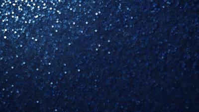 The primary subject of the image is a blue background with a pattern of white stars. The setting appears to be a dark room, and the visual style is a close-up of the blue background with the white stars. The colors and mood of the image are predominantly dark and moody, with the blue background and white stars creating a striking contrast.