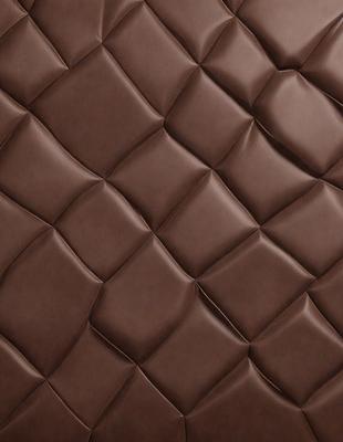 The primary subject of the image is a brown leather couch with a unique pattern on it. The setting is a room with a brown background. The visual style is a close-up of the couch, showcasing its texture and design. The colors and mood of the image are warm and inviting, with the brown leather creating a cozy and comfortable atmosphere.