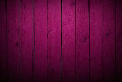The primary subject of the image is a wooden wall with a purple color. The setting is a room with a wooden floor. The visual style is a close-up of the wooden wall, showcasing its texture and color. The dominant colors are purple and brown, creating a warm and inviting atmosphere.