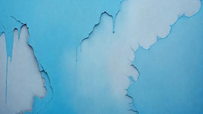 The primary subject of the image is a blue wall with a peeling paint effect. The setting is a room with a blue background. The visual style is a close-up of the wall, showcasing the peeling paint. The colors and mood of the image are predominantly blue, giving it a calm and serene atmosphere.