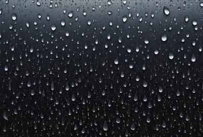 The primary subject of the image is a rainy day, as evidenced by the raindrops falling on a black background. The setting is a dark, rainy environment, and the visual style is a close-up of the raindrops on the black surface. The colors and mood of the image are predominantly dark and moody, with the raindrops creating a sense of wetness and gloominess.