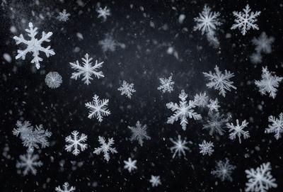 The primary subject of the image is a snowy scene with a dark background. The setting is a winter landscape, possibly a nighttime cityscape, as the snowflakes are falling in the air. The visual style is a black and white photo, which adds a sense of nostalgia and timelessness to the scene. The dominant colors are white and black, creating a stark contrast between the snowflakes and the dark background. The overall atmosphere is serene and peaceful, as the snowflakes gently