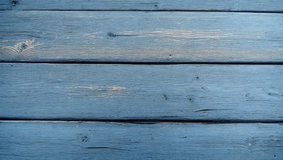 The primary subject of the image is a wooden plank with a blue surface. The setting is a wooden floor, and the visual style is a photo. The dominant colors are blue and brown, creating a calm and natural atmosphere.