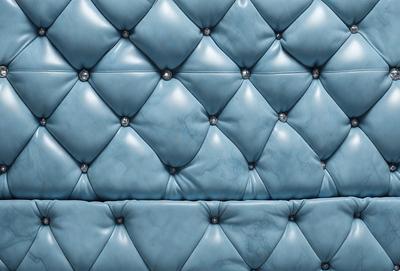 The primary subject of the image is a blue leather couch with a patterned design. The setting is a room with a blue background, and the visual style appears to be a photo. The dominant colors in the image are blue and white, creating a calm and relaxing atmosphere.