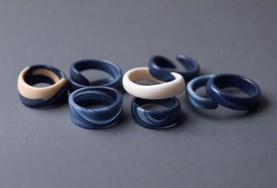 The primary subject of the image is a collection of various colored rings. The rings are arranged on a grey surface, which serves as the setting or background. The visual style of the image is a close-up of the rings, showcasing their colors and details. The dominant colors in the image are shades of blue and grey, creating a calm and sophisticated atmosphere.