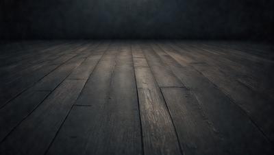 The primary subject of the image is a wooden floor. The setting is a dark room, and the visual style is a black and white photo. The colors and mood of the image are predominantly dark and moody, with the wooden floor being the main focus.
