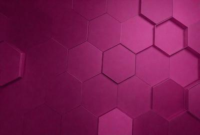The primary subject of the image is a purple wall with a pattern of hexagons. The setting is a room with a pink wall, and the visual style is a close-up of the wall. The dominant colors are purple and pink, creating a warm and inviting atmosphere.