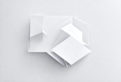 The image features a white paper with a geometric pattern, possibly a cube or a diamond shape. The paper is placed on a white surface, which could be a wall or a table. The overall atmosphere of the image is clean and minimalistic, with the focus on the geometric pattern and the white paper.