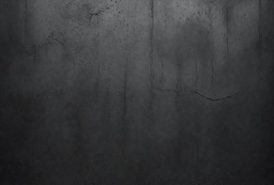 The primary subject of the image is a large, dark grey wall with a rough texture. The setting is a room with a concrete surface, which adds to the overall atmosphere. The visual style is a close-up of the wall, showcasing its texture and color. The dominant colors are grey and black, creating a moody and dramatic ambiance.