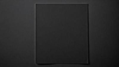 The primary subject of the image is a square-shaped piece of black paper. The setting is a black background, which creates a stark contrast with the paper. The visual style is a simple, minimalist design. The colors and mood are predominantly dark and moody, with the black paper being the main focus of the image.