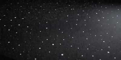 The primary subject of the image is a black background with white specks or dots scattered across it. The setting appears to be a dark room, and the visual style is a close-up of the black background with the white specks. The colors and mood of the image are predominantly dark and moody, with the white specks adding a touch of contrast and interest to the overall composition.
