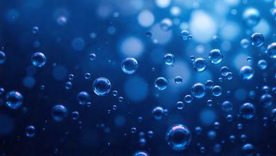 The primary subject of the image is a blue background with numerous small bubbles floating in the air. The setting appears to be a dark, possibly nighttime, environment. The visual style of the image is a close-up of the bubbles, creating a sense of depth and detail. The colors in the image are predominantly blue, giving the scene a calm and serene atmosphere.