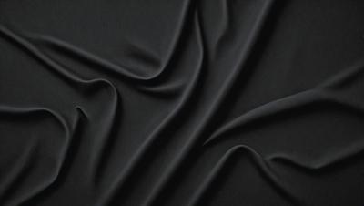 The primary subject of the image is a close-up of a black fabric, possibly a piece of clothing or a curtain. The setting is a dark background, which emphasizes the fabric's texture and pattern. The visual style appears to be a photo, as it captures the details of the fabric. The colors and mood of the image are predominantly dark, with the black fabric being the main focus.