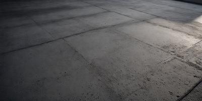 The primary subject of the image is a large, dirty, and worn-out concrete floor. The setting is an outdoor area, possibly a parking lot or a similar location. The visual style of the image is a black and white photo, which adds a sense of age and history to the scene. The colors and mood of the image are dark and moody, emphasizing the worn-out and dirty appearance of the concrete floor.