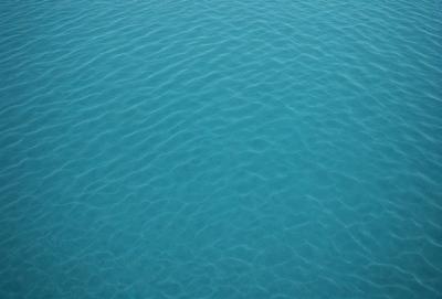 The primary subject of the image is a large body of blue water, which appears to be a lake or a deep blue ocean. The water is calm and serene, with no visible disturbances or waves. The setting is a vast expanse of water, with no visible land or shoreline. The visual style of the image is a close-up of the water, showcasing its depth and tranquility. The colors and mood of the image are predominantly blue, creating a sense of calmness and relaxation