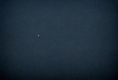 The primary subject of the image is a small light in the sky, which appears to be a star. The setting is a dark, cloudy night sky, with no other objects or people visible. The visual style is a black and white photo, which adds a sense of drama and timelessness to the scene. The colors and mood of the image are predominantly dark and moody, with the star being the only source of light in the otherwise dark and cloudy sky.