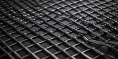 The primary subject of the image is a close-up of a black mesh or woven material. The setting is a black background, which provides a stark contrast to the mesh. The visual style is a detailed, up-close view of the mesh, showcasing its intricate pattern. The colors and mood of the image are predominantly dark, with the black mesh and background creating a moody atmosphere.