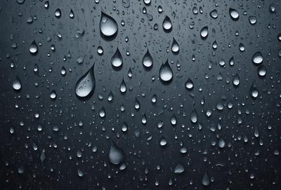 The primary subject of the image is a rainy day, as evidenced by the numerous droplets of water on a black background. The setting is a dark, cloudy sky, and the visual style is a close-up of the raindrops. The colors and mood of the image are predominantly dark and moody, with the raindrops creating a sense of depth and texture.