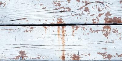 The primary subject of the image is a wooden bench with a rusty surface. The setting is outdoors, with the bench placed on a wooden deck. The visual style is a photo, capturing the rusty appearance of the bench. The colors and mood of the image are predominantly brown and rusty, creating a sense of age and weathering.