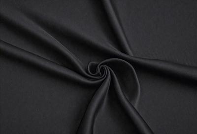 The primary subject of the image is a black fabric, which is the main object, scene, or focus of the image. The setting or background is a dark background, which complements the black fabric. The visual style of the image is a close-up of the fabric, showcasing its texture and details. The colors and mood of the image are predominantly dark, with the black fabric being the dominant color, creating a moody and dramatic atmosphere.