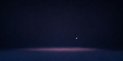 The primary subject of the image is a moon, which is the main object in the scene. The setting is a dark sky, with the moon being the only visible light source. The visual style is a photo, capturing the moon in its natural environment. The colors and mood of the image are predominantly dark and moody, with the moon being the only bright spot in the sky.