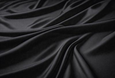 The primary subject of the image is a black fabric, which is the main object, scene, or focus of the image. The setting or background is a dark room, and the visual style is a close-up of the fabric. The colors and mood of the image are predominantly dark and moody, with the black fabric being the dominant color.