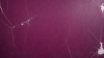 The primary subject of the image is a purple leather surface with a crack in it. The setting is a wall, and the visual style is a close-up of the leather surface. The colors and mood of the image are dominated by the purple hue, giving it a rich and luxurious appearance.