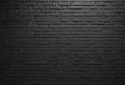 The primary subject of the image is a brick wall. The setting is a dark room, and the visual style is a black and white photo. The dominant colors are black and white, creating a moody atmosphere.