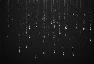 The primary subject of the image is a series of raindrops falling from the sky. The setting is a black background, which creates a dramatic contrast with the raindrops. The visual style is a close-up of the raindrops, emphasizing their individual shapes and sizes. The colors and mood of the image are predominantly dark, with the raindrops being the main focus and creating a sense of movement and fluidity.