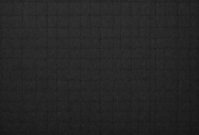 The primary subject of the image is a black background with a pattern of small squares. The setting is a dark room, and the visual style is a close-up of the pattern. The colors and mood are predominantly dark and moody, with the black background and pattern creating a sense of depth and intrigue.