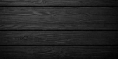The primary subject of the image is a wooden surface, possibly a wooden floor or a wooden wall. The setting is a dark room, which creates a moody atmosphere. The visual style is a black and white photo, giving the image a classic and timeless appearance. The colors and mood are predominantly dark, with the wooden surface being the main focus of the image.