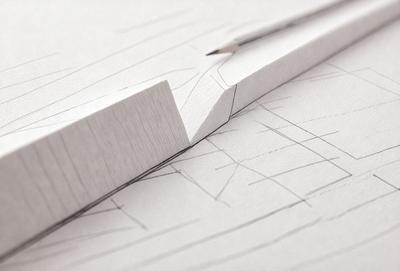 The primary subject of the image is a pencil, which is placed on a piece of paper. The setting is a desk, and the visual style appears to be a drawing or illustration. The colors and mood of the image are predominantly white, giving it a clean and minimalist appearance.