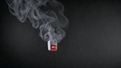 The primary subject of the image is a small red box, which is the main focus of the scene. The setting is a dark background, which creates a dramatic and moody atmosphere. The visual style of the image is a combination of photo and digital art, as it appears to be a close-up of the red box with smoke surrounding it. The colors in the image are predominantly dark, with the red box being the only bright and noticeable element.