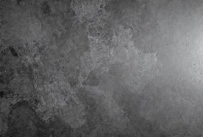 The primary subject of the image is a large, textured surface with a gray color. The setting is a concrete wall, and the visual style is a close-up of the wall. The colors and mood of the image are predominantly gray, giving it a somewhat dull and industrial appearance.